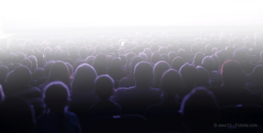 People sitting in an audience facing a bright light